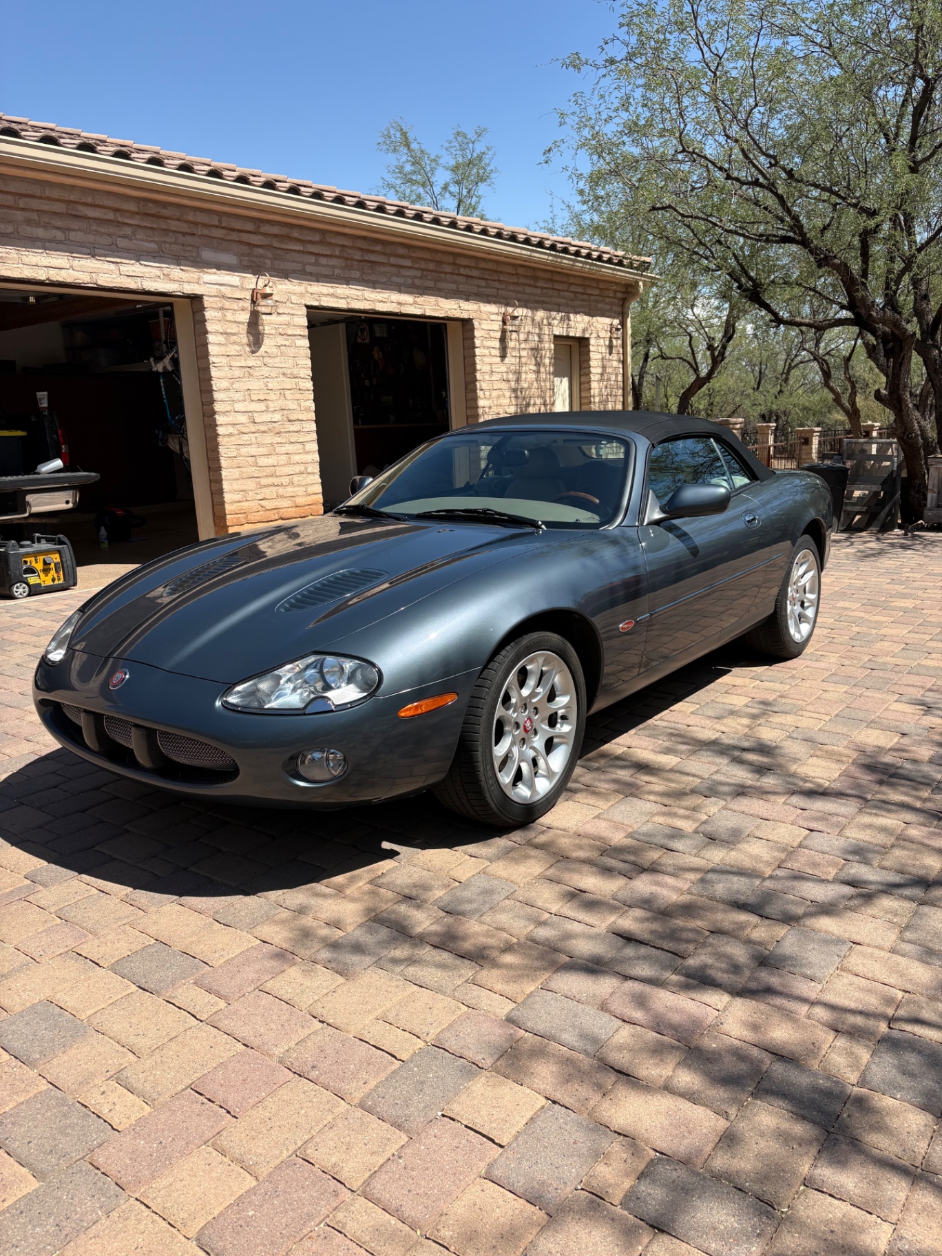A detailed gray Jaguar convertible parked on a Tucson paver driveway in the desert sun